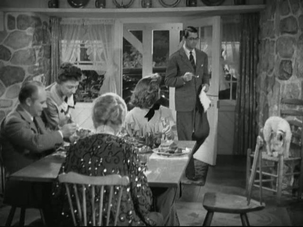 Cary Grant standing beside dining table 