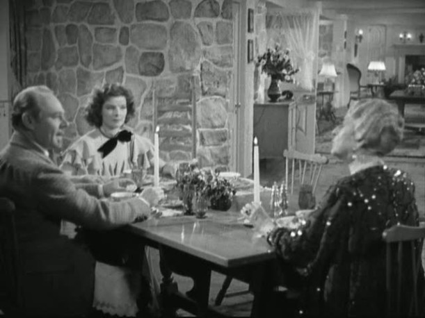 Katharine Hepburn at head of dining table with stone wall 