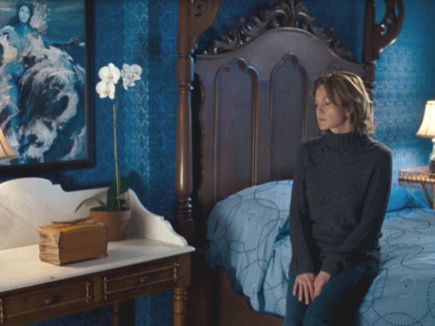 Diane Lane sitting on a bed in the blue bedroom