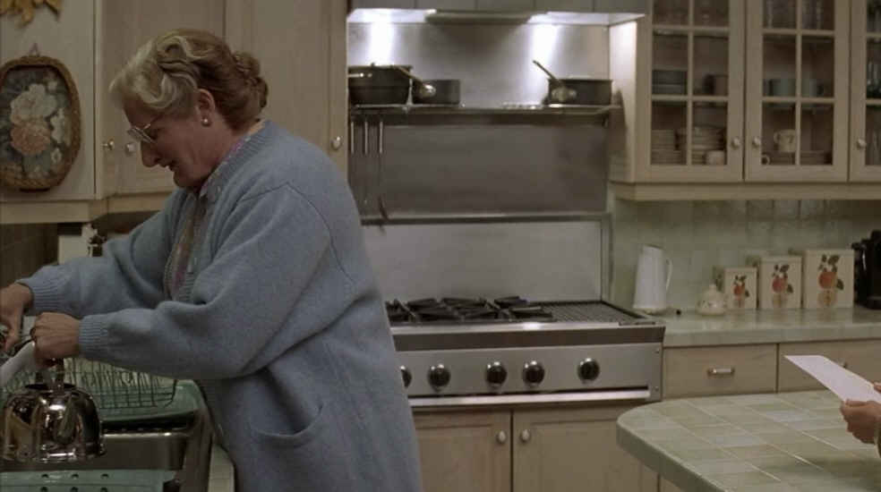 Mrs. Doubtfire standing in the kitchen by the sink