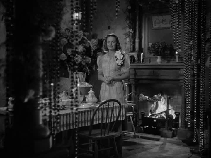 Mary Bailey stands in front of table beside fireplace