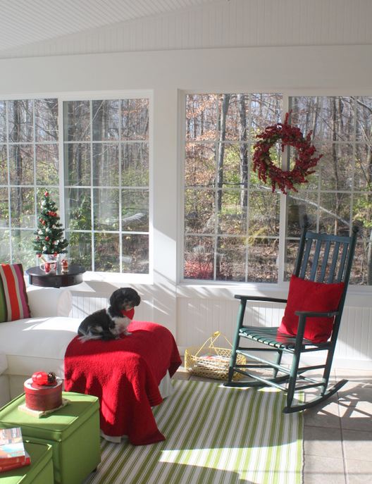 sunroom decorated for Christmas in red and green with dog on sofa