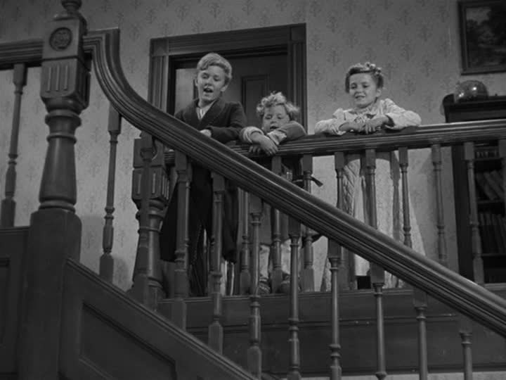 three children looking over stair railing on landing