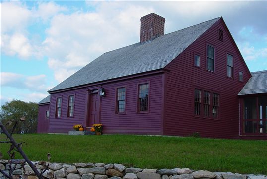 A dark red cape style home built to look older than it is