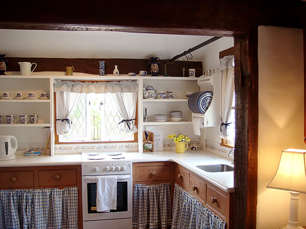 A kitchen with skirted sink and open shelves in cottage