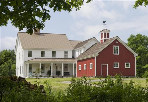 exterior of white house with front porch beside red barn