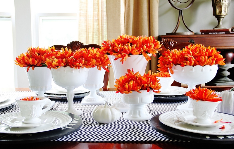 A table topped with plates, vases and orange flowers for fall