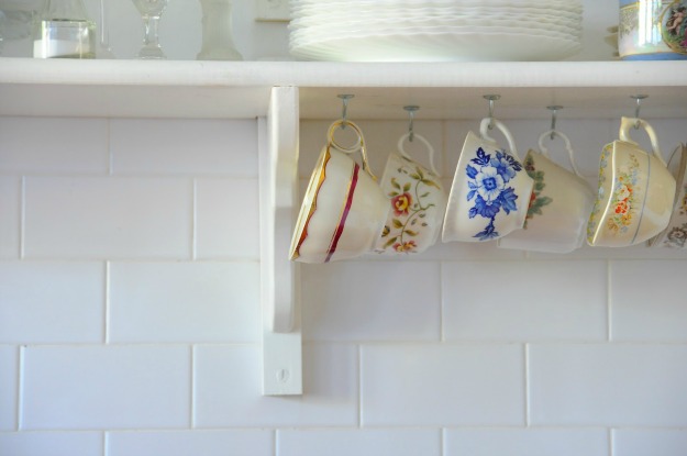 closeup of teacups hanging from hooks under kitchen shelf