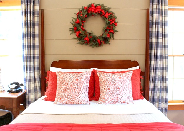 A bedroom with red and white bedding and Christmas wreath over headboard