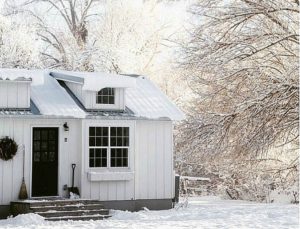 A little white house with black door covered in snow