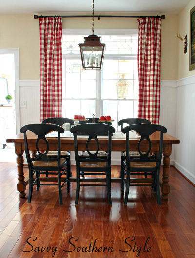 A dining room table with red and white checked curtains