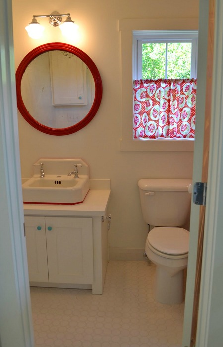 small bathroom with round red mirror over sink