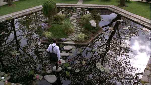 Sabrina\'s father walking across the stone bridge over the koi pond