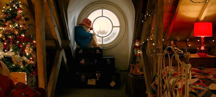 Paddington sits in round window on stack of suitcases