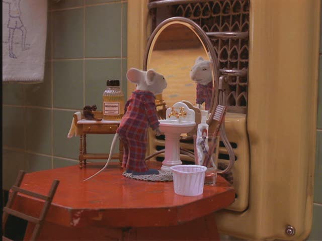 Stuart Little in the bathroom standing in front of his tiny sink and mirror