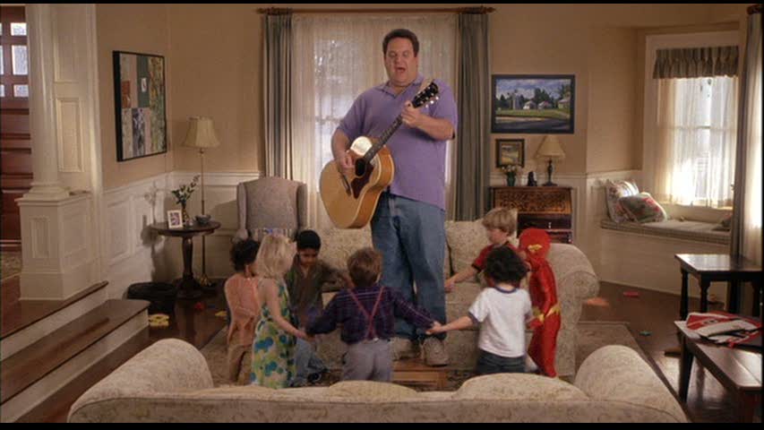 man playing guitar while children hold hands in circle in living room