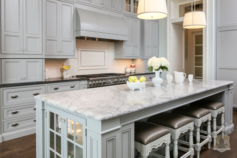 pale blue kitchen with vent hood over range and vase of flowers on island