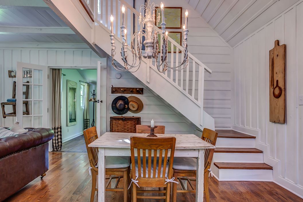 white kitchen table, wood chairs, white chandelier, and stairs to upper floor