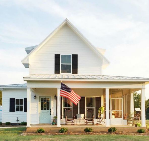 Front exterior of white farmhouse with black shutters and blue door