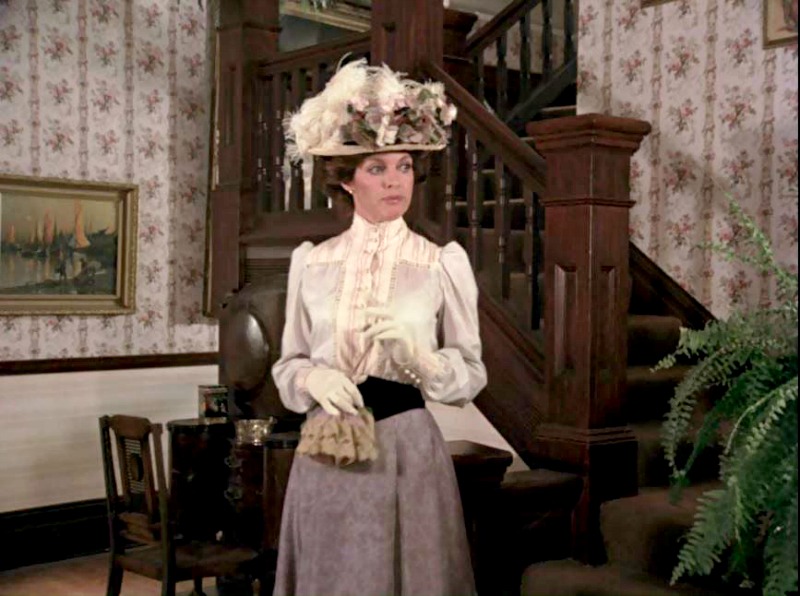 Woman in Victorian garb and hat at base of staircase