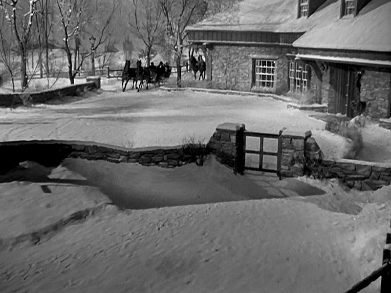 The farmhouse covered in snow with horse pulling a sleigh up the drive