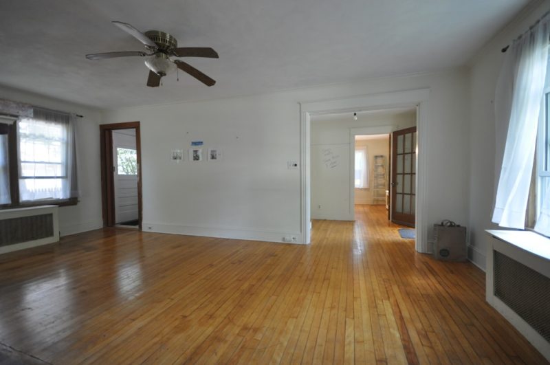 A large empty room with a hard wood floor before remodel