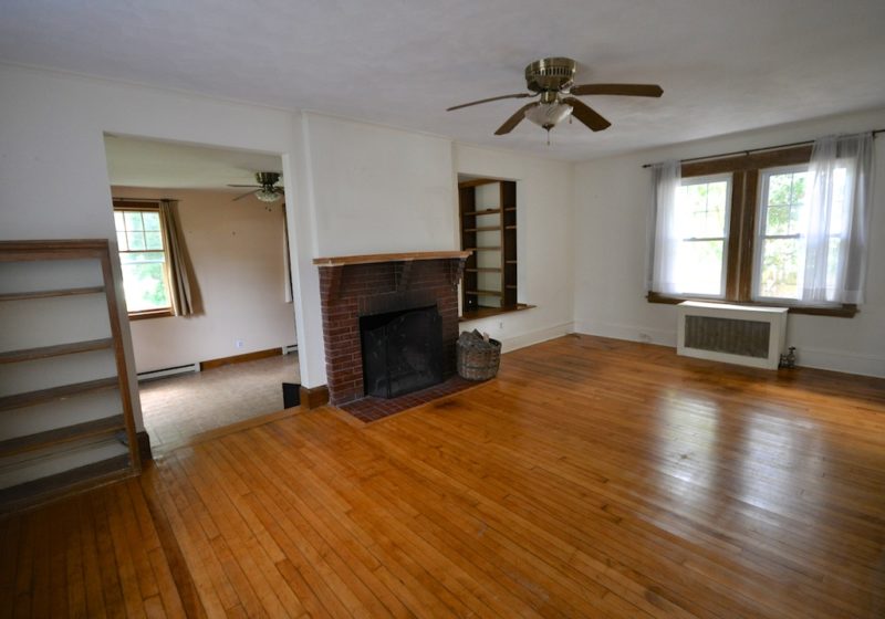 A view of a living room with a hard wood floor before remodel