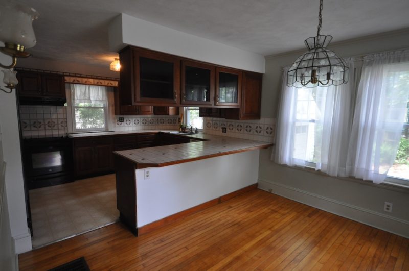 A kitchen with hard wood floors and a large window before remodel