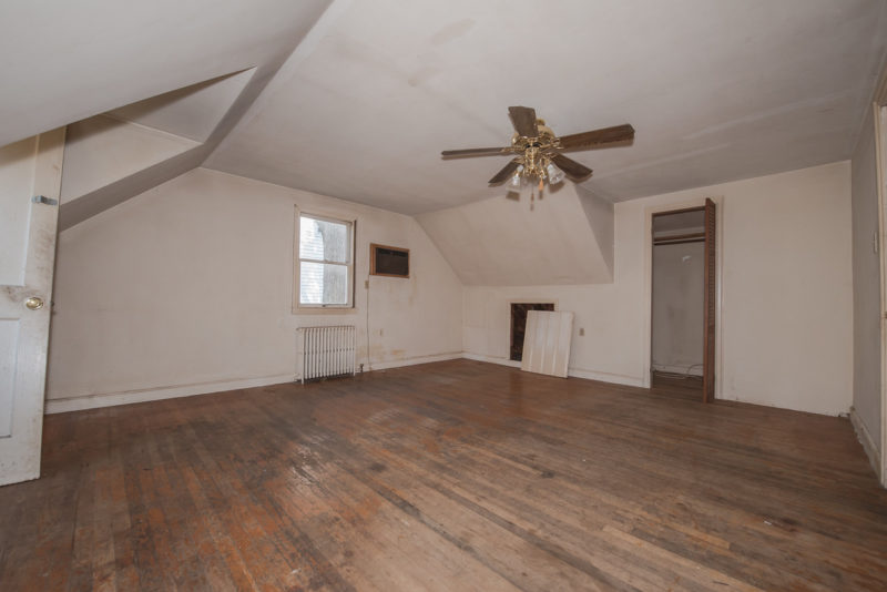 A large empty room with a wood floor before remodel