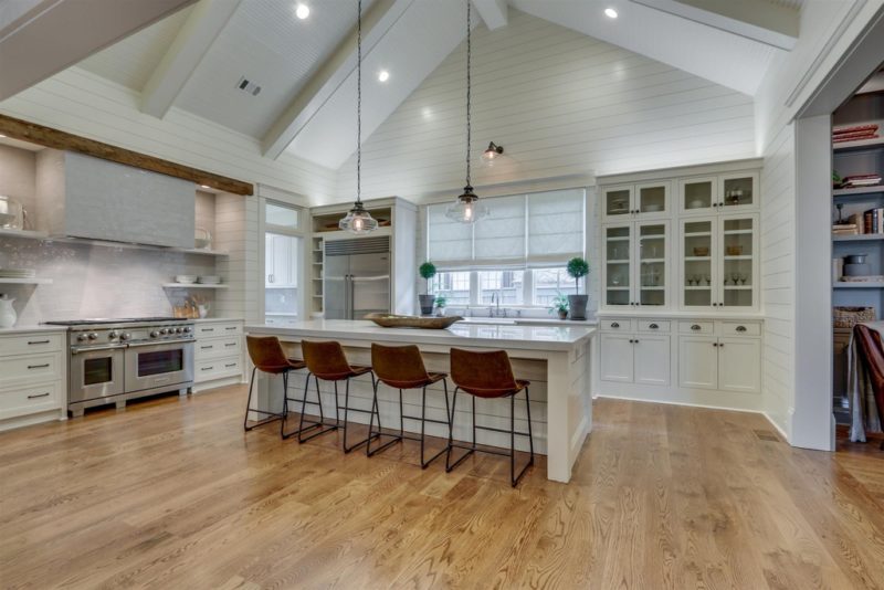 A kitchen with a hard wood floor, vaulted ceiling, and white cabinets