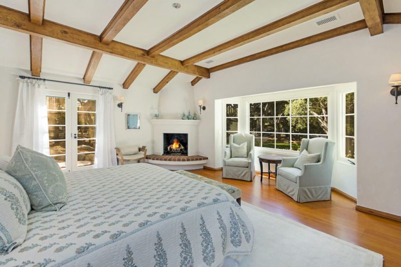 A bedroom with corner fireplace and beamed ceiling