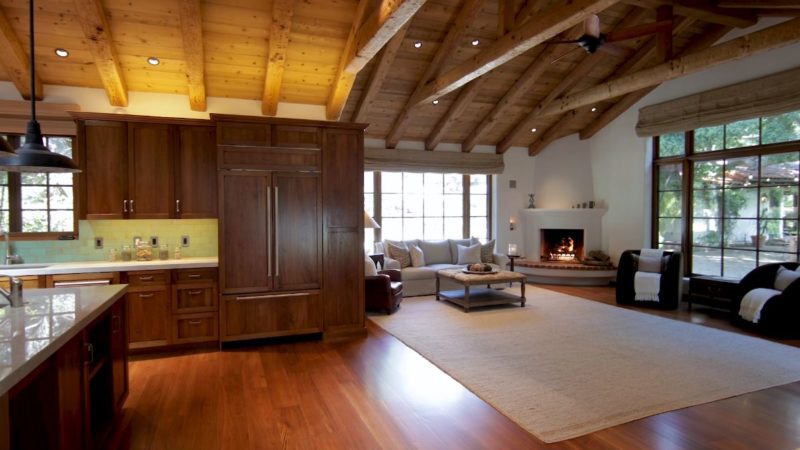 A kitchen with wooden cabinets open to family room with corner fireplace