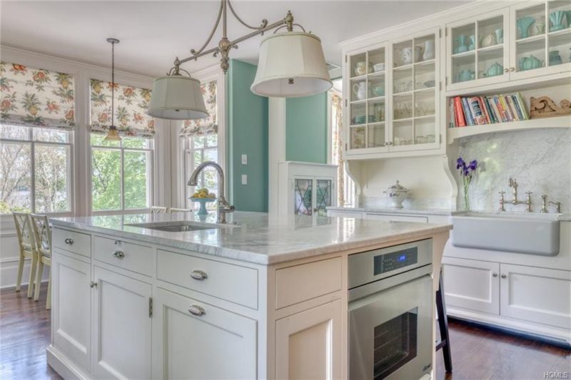 A kitchen with a large white island, marble countertop, and sink