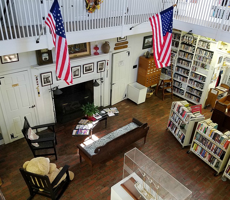 Inside Beach Haven Public Library with bookshelves, two American flags and fireplace