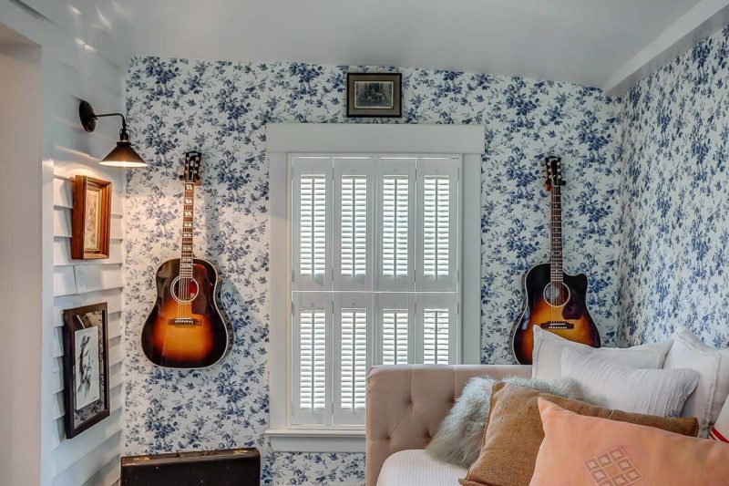 Two guitars hanging on wallpapered wall