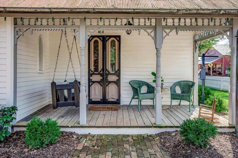 Front porch of Sweeney Cottage with double doors painted pick and porch swing