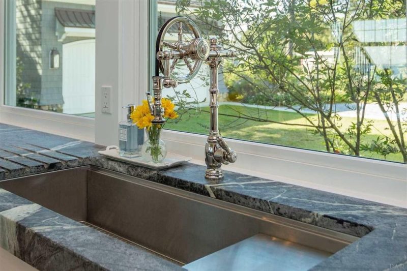 Vase with yellow flowers on windowsill behind sink faucet